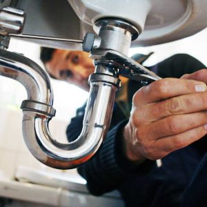 a plumber with a wrench trying to open the sink pipe